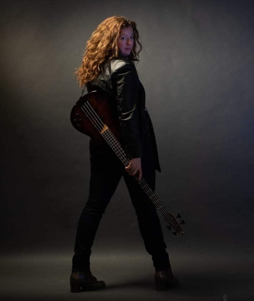 Female musician holding guitar, standing in a dark studio setting.
